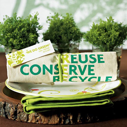 A wedding table place setting with green plants and a reusable tote bag tied up with string. The words Reuse, conserve and recycle are displayed on the bag.