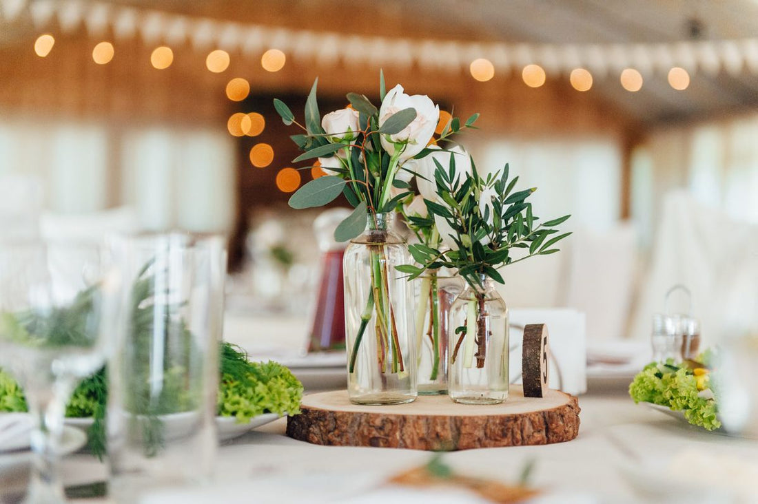 A wedding banquet table with upcycled glass vases with eucalyptus in them arranged on a slice of wood log