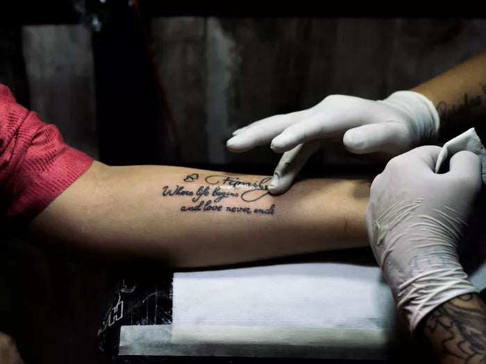 A person's forearm with a gloved tattoo artist finishing up a meaningful saying.