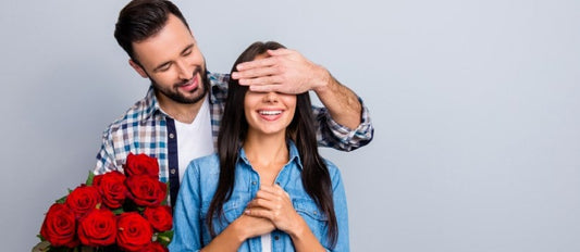 Man standing behind woman with a bouquet of red roses in one hand, covering her eyes with his other hand